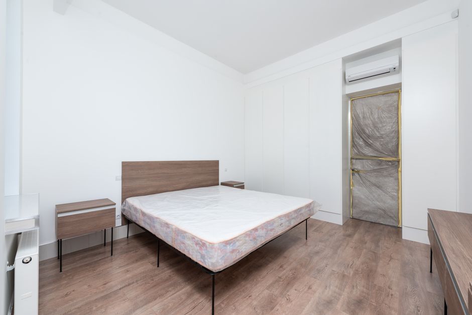Spacious minimalist bedroom featuring a large bed, sleek furniture, and wooden flooring.