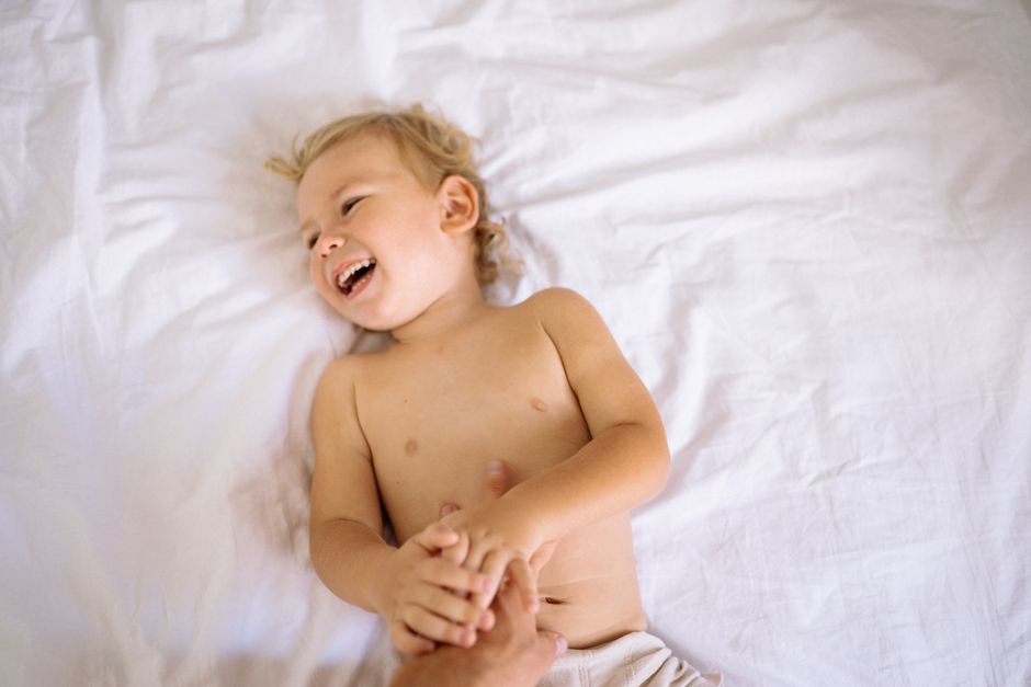 A happy child laughing playfully while lying on a comfortable white bed.
