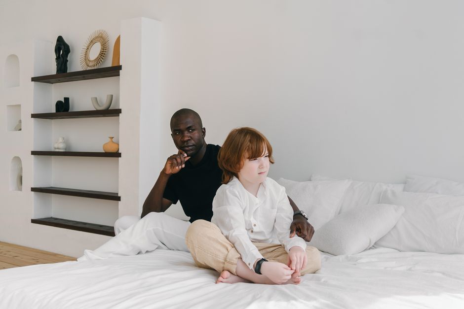 A father comforts his son in a modern, minimalist bedroom setting.